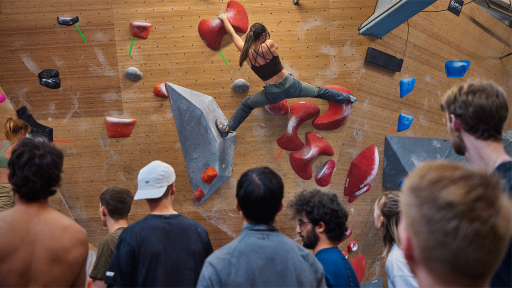 girl climbing in colorfuld bouldering gym with in front of onlooking crowd